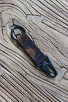 Nahaufnahme eines Leder Schlüsselanhängers in Camouflage mit einem Karabiner und Schlüsselring in Schwarz auf einem Holzstuhl.