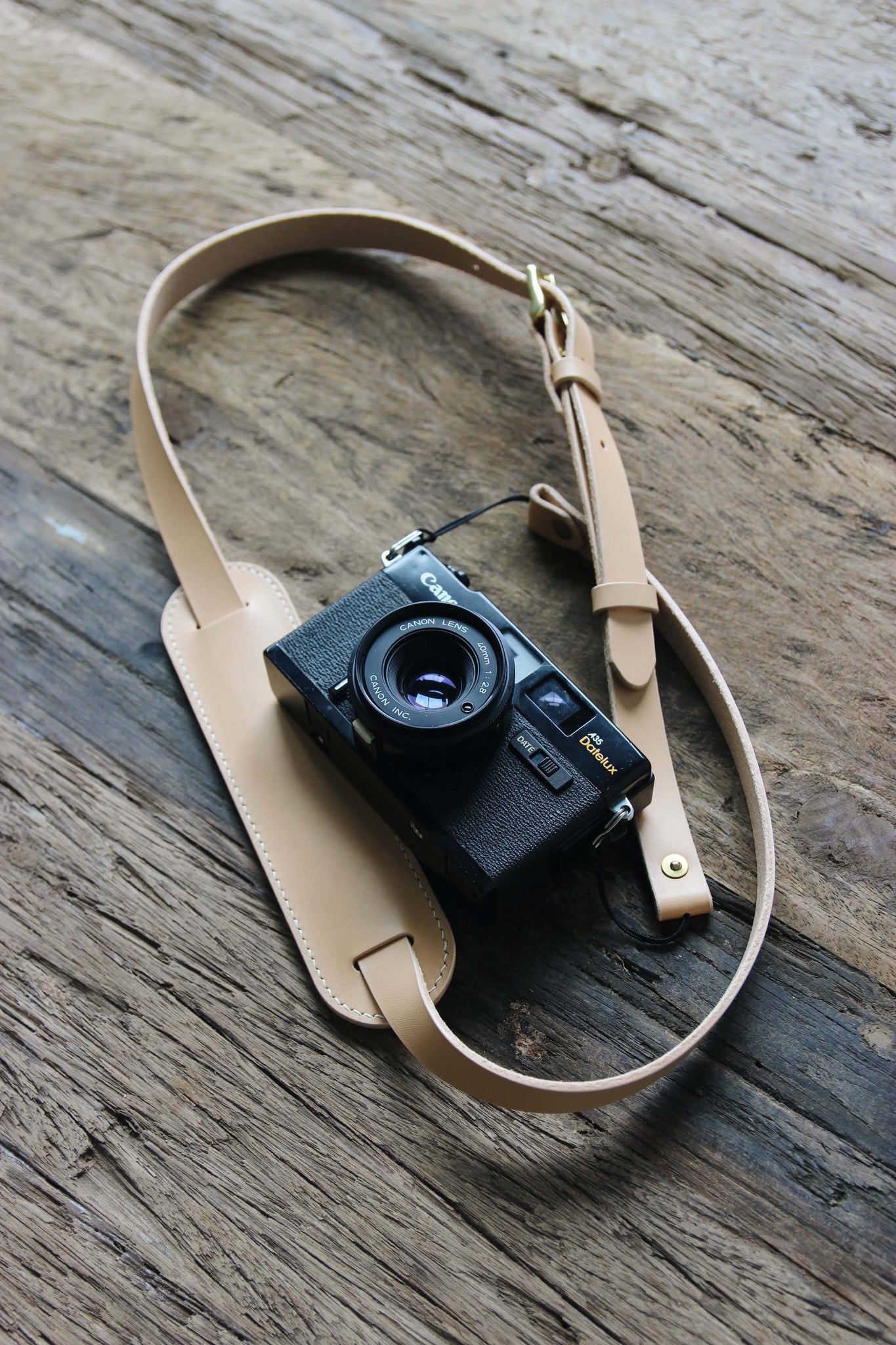 Eine Kamera mit einem Leder Kameragurt in Natural auf einem Holztisch liegend.