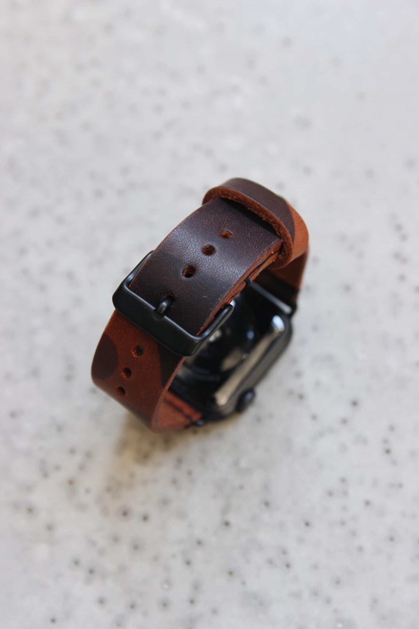 Eine Apple Watch mit einem Lederband in Camo auf einem Betonboden stehend.