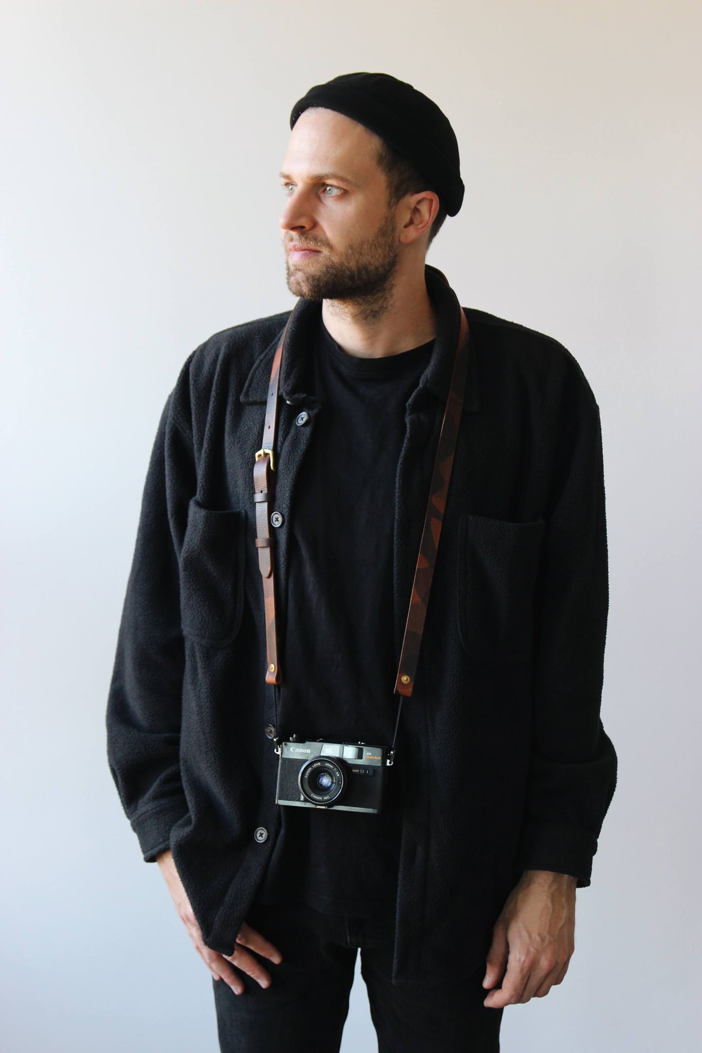 Ein Mann mit schwarzer Kleidung trägt eine Kamera mit einem Leder Kameragurt in Camouflage um den Hals.