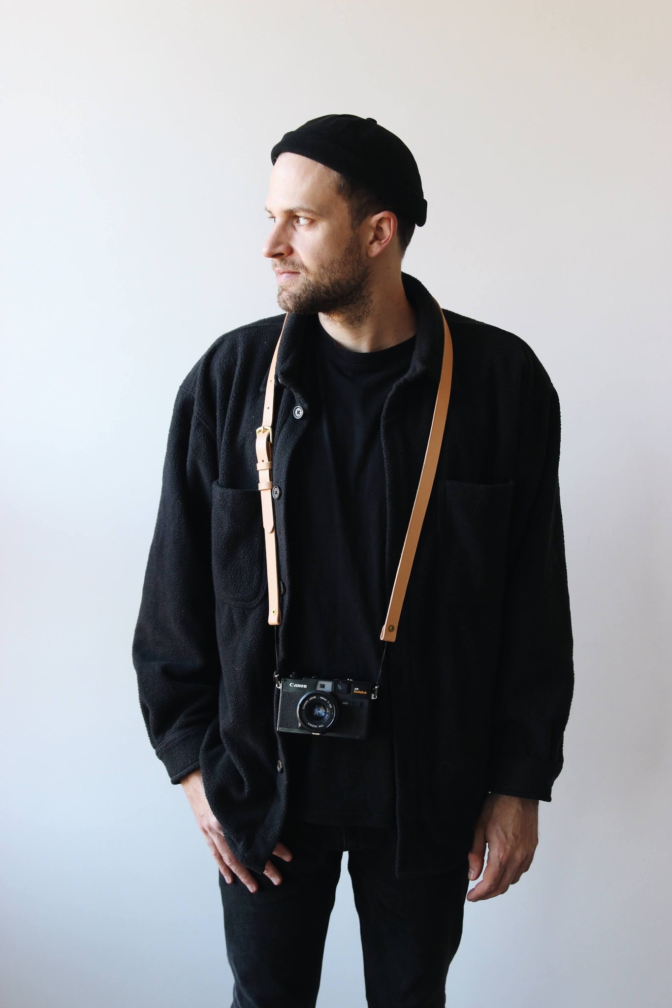 Ein Mann mit schwarzer Kleidung trägt eine Kamera mit einem Leder Kameragurt in Natural um den Hals.