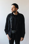 Ein Mann mit schwarzer Kleidung trägt eine Kamera mit einem Leder Kameragurt in Schwarz um den Hals.