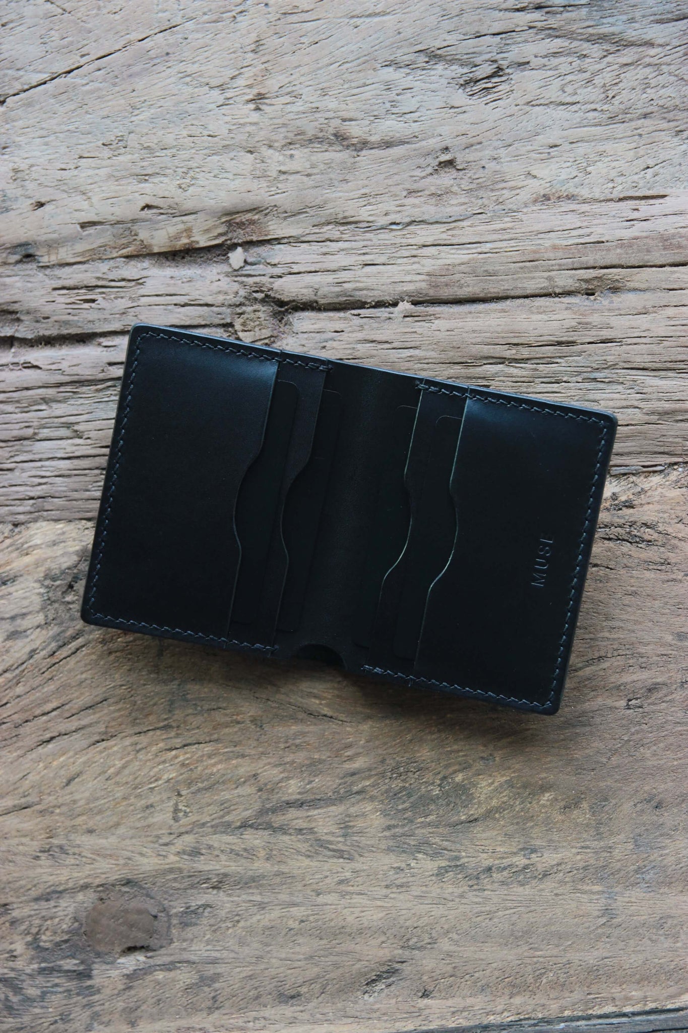 Draufsicht auf ein Leder Kartenetui in Schwarz auf einer Holzplatte liegend.