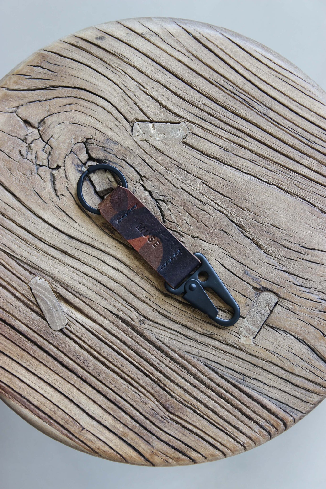 Ein Leder Schlüsselanhänger in Camouflage mit einem Karabiner und Schlüsselring in Schwarz auf einem Holzstuhl.