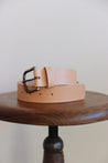 Ledergürtel für Herren in Natural zusammengerollt auf einem Stuhl mit einer Sitzfläche aus Holz.