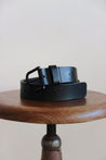 Ledergürtel für Herren in Schwarz zusammengerollt auf einem Stuhl mit einer Sitzfläche aus Holz.