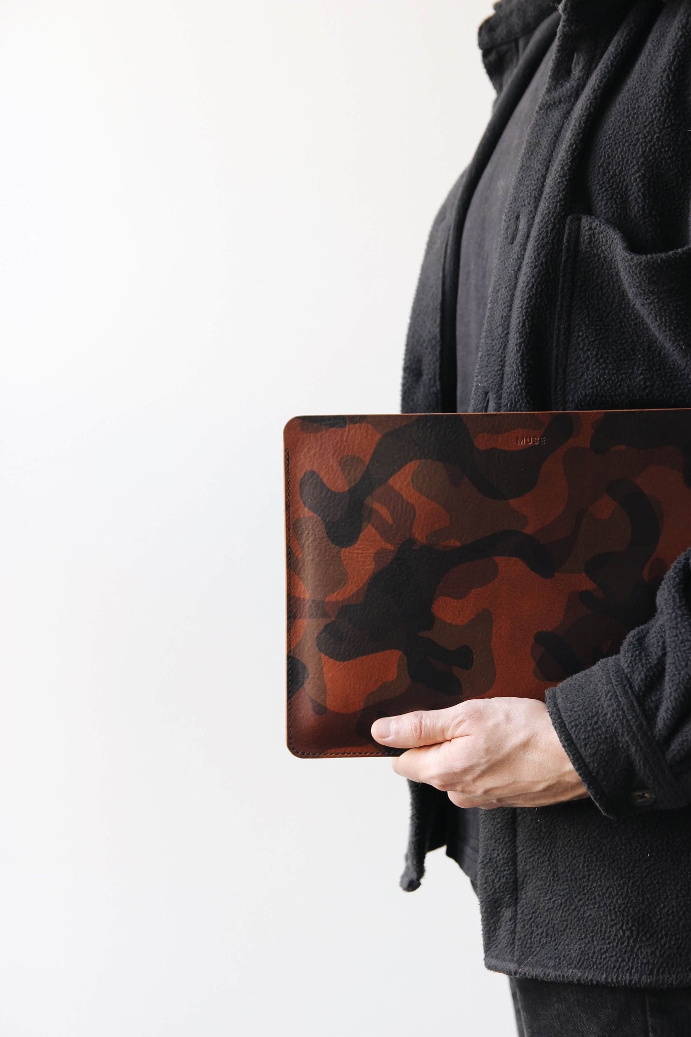 Eine Leder MacBook Hülle in Camouflage wird von jemandem in schwarzer Kleidung in der Hand gehalten.