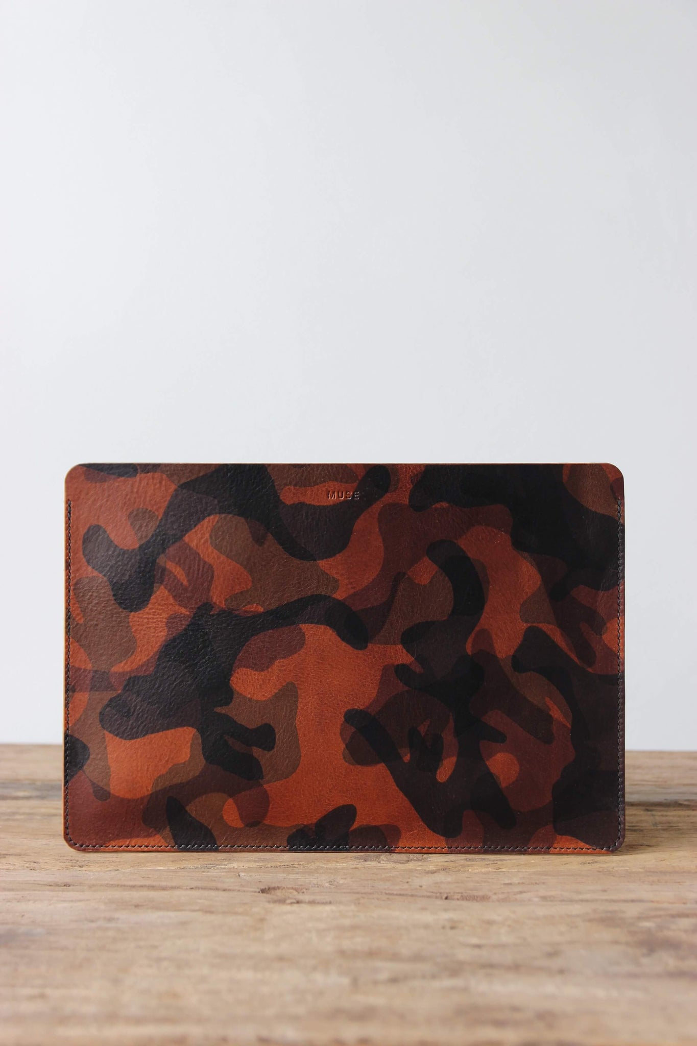 Eine Leder MacBook Hülle in Camouflage steht auf einem Holztisch.
